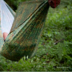 someone laying down in a chameleon hammock in the woods
