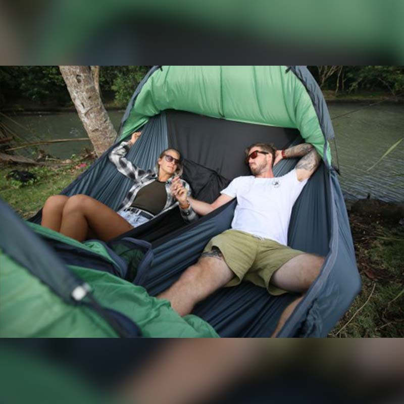 a man and a woman laying down in a double person camping hammock